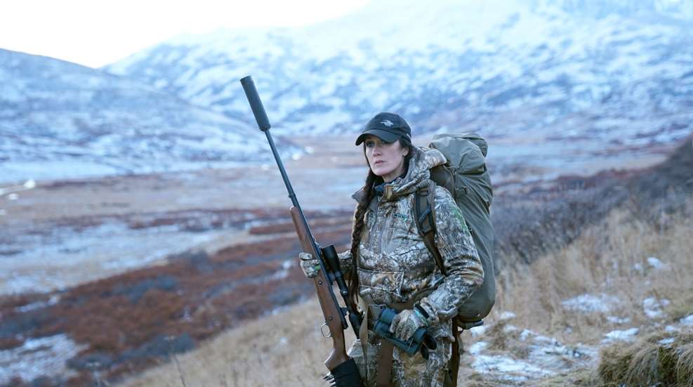 Melissa Bachman carrying suppressed rifle in snow covered mountains